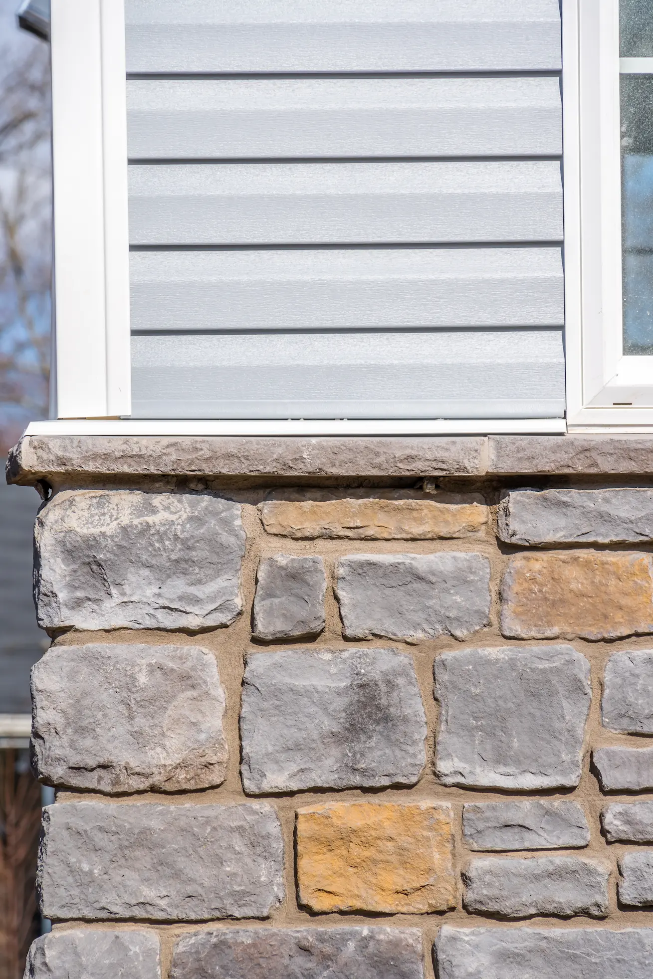 Contact Us Light gray vinyl siding and stacked stone foundation on a house exterior.